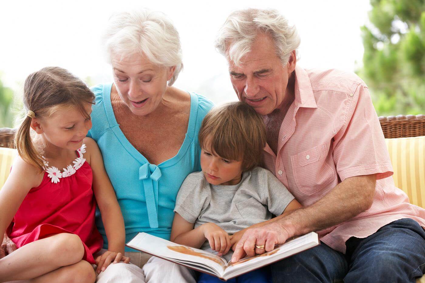Großeltern und Enkelkinder lesen ein Buch auf einem Gartensitzplatz